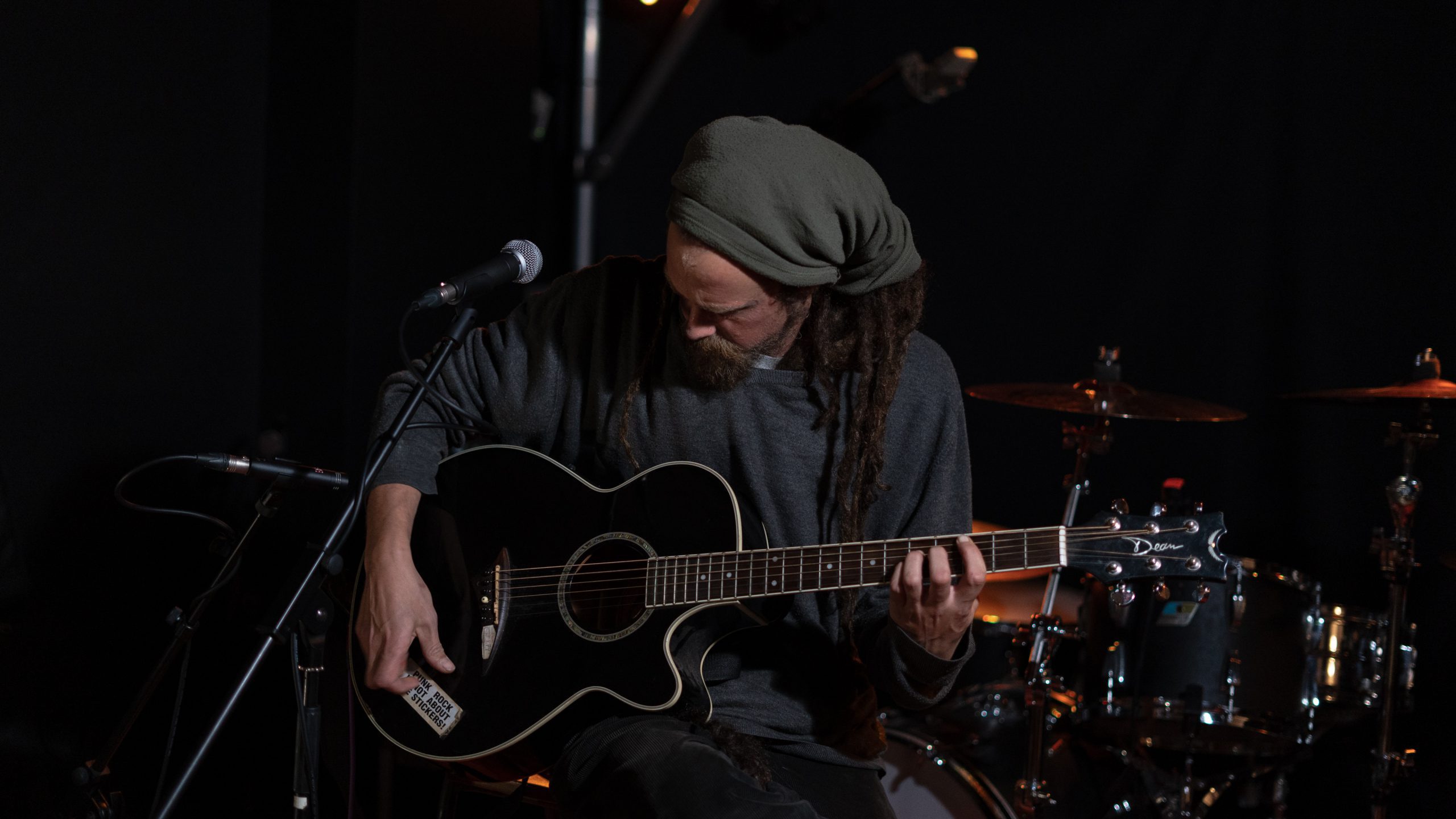 Man with dreadlocks and a head scarf playing guitar on darkened stage