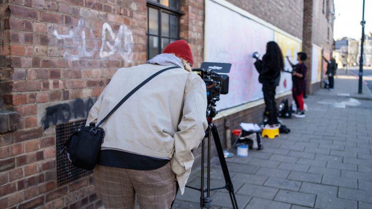 A man filming people on a street painting on a billboard