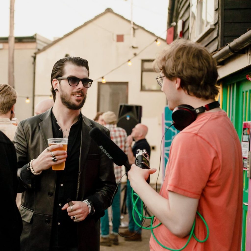 A man holding a microphone to another man's mouth who is drinking a beer.