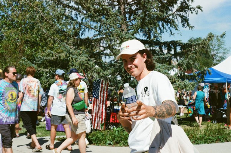 Man in a sunny, treed environment pointing to the camera whilst holding a water bottle.