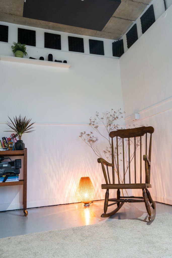 Image of a rocking chair in the corner of a fresh, clean and open space warmly lit by a small lamp.