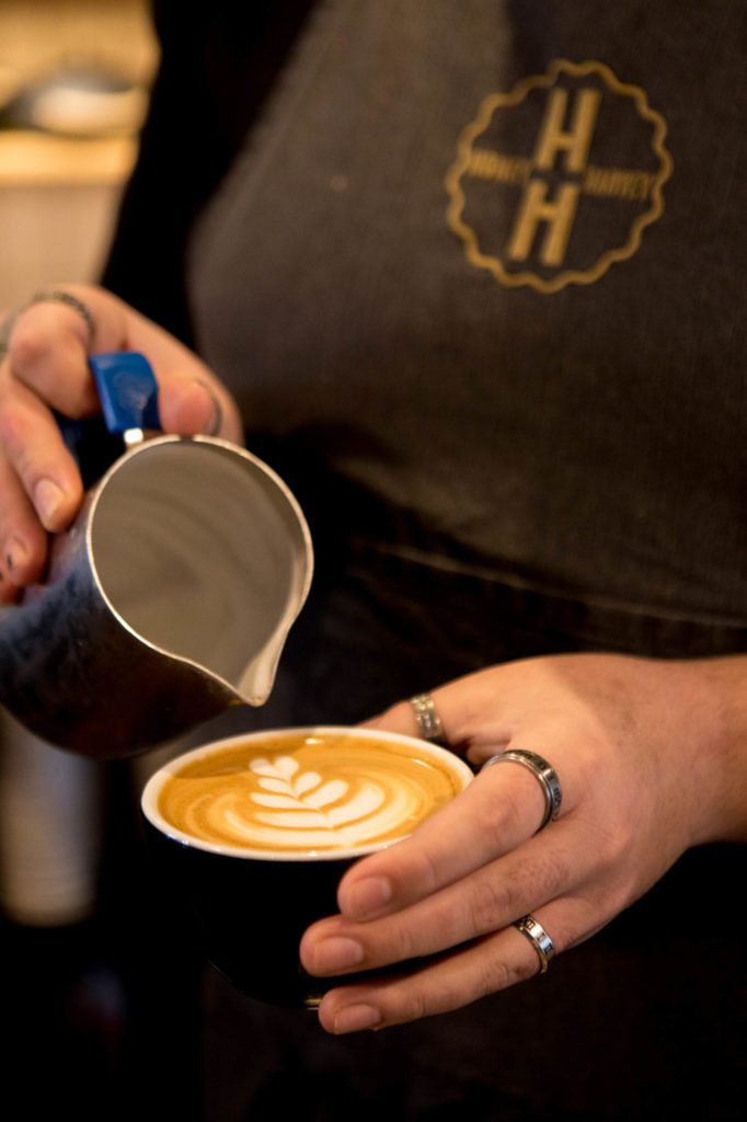 A barista performing coffee art, pouring decorative milk into a latte.