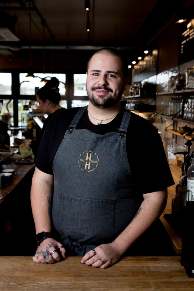 A gentleman working as a barista, wearing a Honey and Harvey apron, photographed in a cafe in Melton, Suffolk.